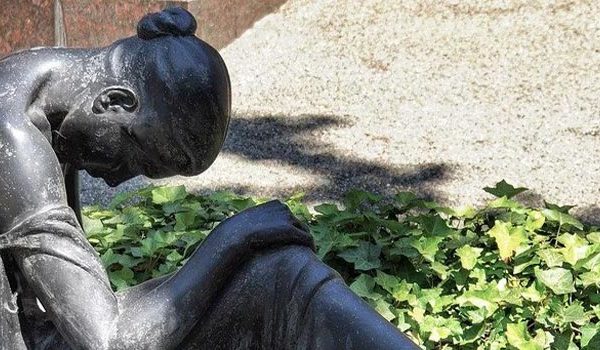 Grave of a woman looking down next to greenery