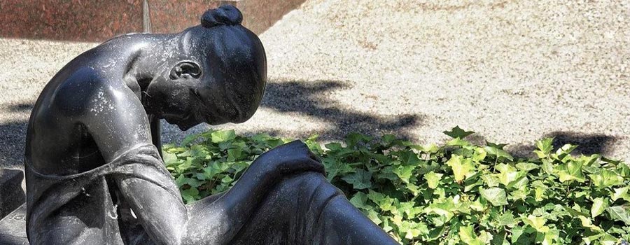 Grave of a woman looking down next to greenery