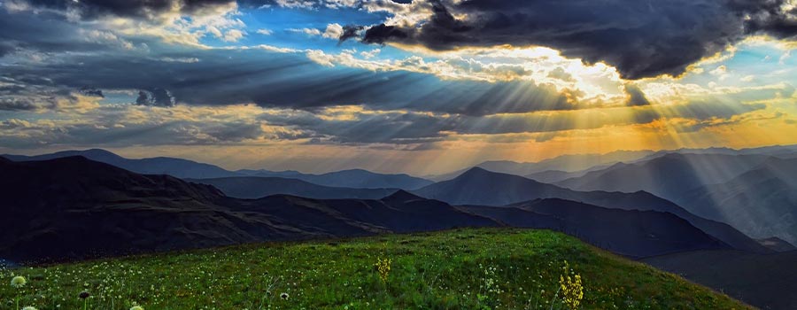 Landscape photo of mountains with the sun poking through the clouds