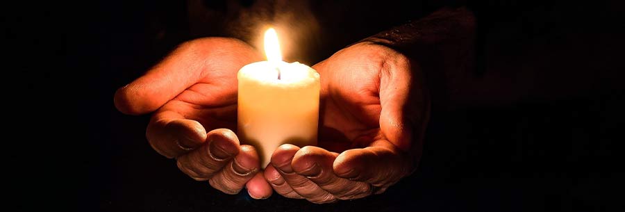 Person holding a candle in their hands in a dark room