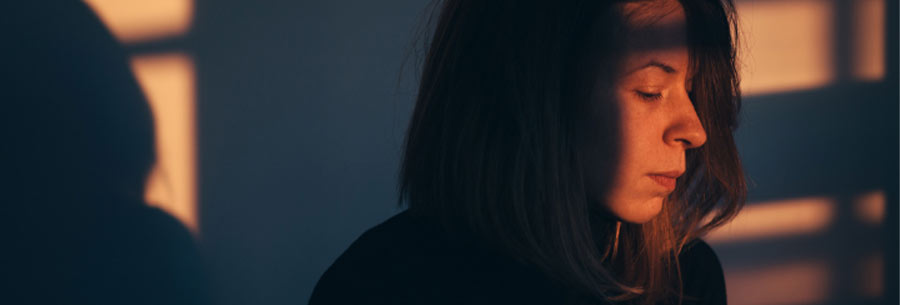 Woman looking down grieving in sunlit room