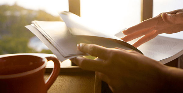 Person drinking coffee and reading book at sunset