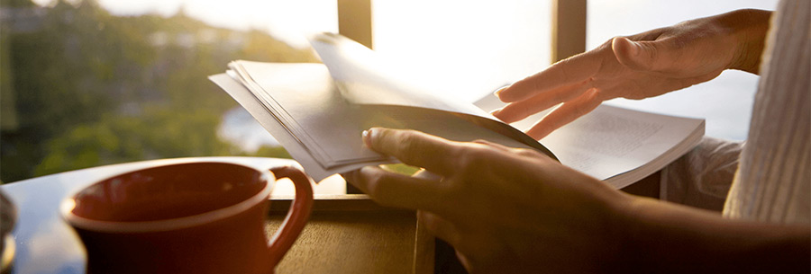 Person drinking coffee and reading book at sunset