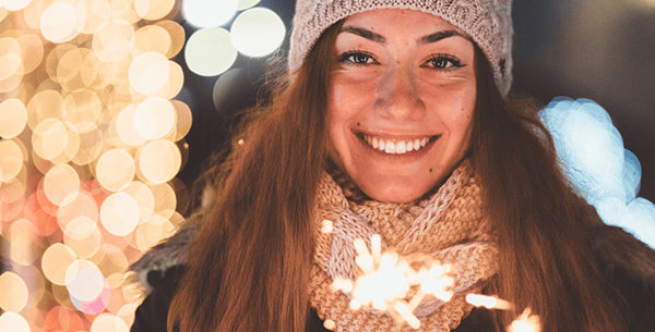 Person holding sparkler outside with Holiday lights in background