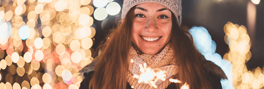 Person holding sparkler outside with Holiday lights in background